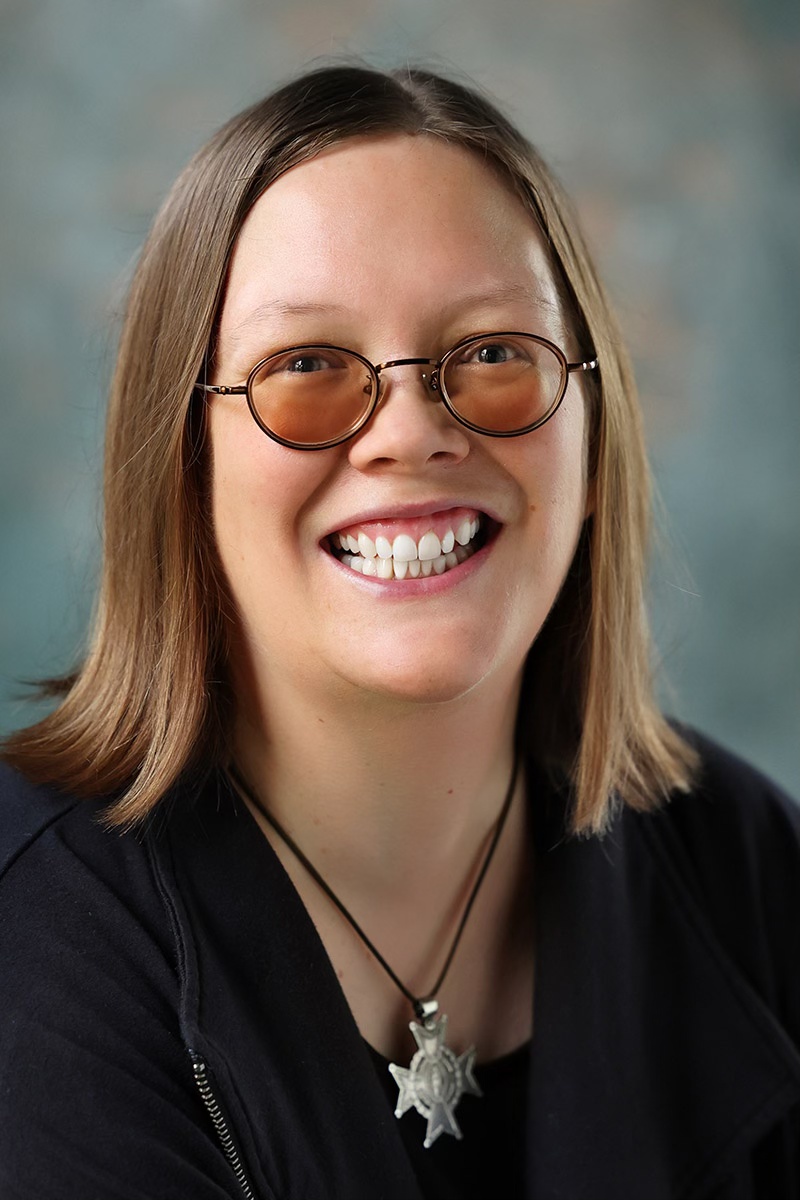 woman with tinted glasses and blond hair and cross necklace smiling