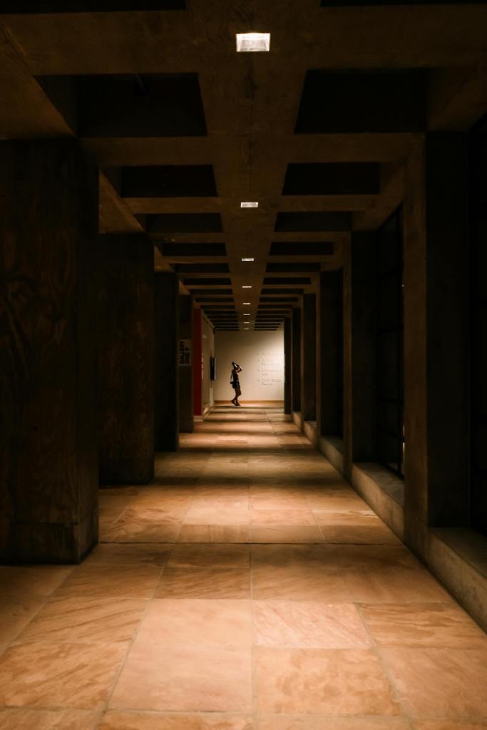 A moody, dimly lit corridor with a solitary figure standing at the end, Tempe, AZ.
