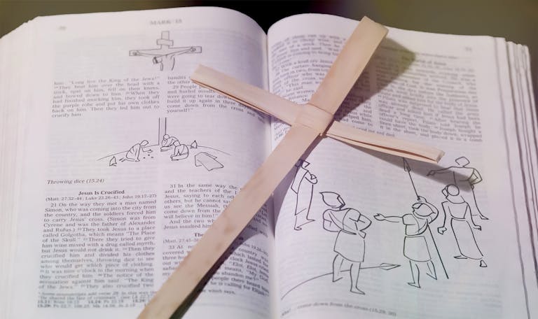 Bible open to crucifixion passage with wooden cross placed on top, symbolizing Christian faith.