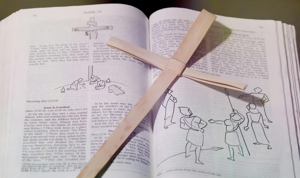 Bible open to crucifixion passage with wooden cross placed on top, symbolizing Christian faith.